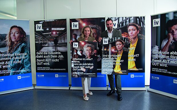 Zwei Personen, IV-NÖ-Geschäftsführerin Michaela Roither (links) und IV-NÖ-Präsident Kari Ochsner (rechts) stehen vor fünf aufgestellten Roll-Ups mit Botschaften der IV-Kampagne „Damit AUT nicht OUT wird“; sie halten jeweils ein Plakat mit Kampagnensujet in den Händen. Die Plakate zeigen unterschiedliche gesellschaftliche und wirtschaftliche Themen rund um Industrie, Arbeit und Standortpolitik.