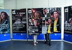 Zwei Personen, IV-NÖ-Geschäftsführerin Michaela Roither (links) und IV-NÖ-Präsident Kari Ochsner (rechts) stehen vor fünf aufgestellten Roll-Ups mit Botschaften der IV-Kampagne „Damit AUT nicht OUT wird“; sie halten jeweils ein Plakat mit Kampagnensujet in den Händen. Die Plakate zeigen unterschiedliche gesellschaftliche und wirtschaftliche Themen rund um Industrie, Arbeit und Standortpolitik.