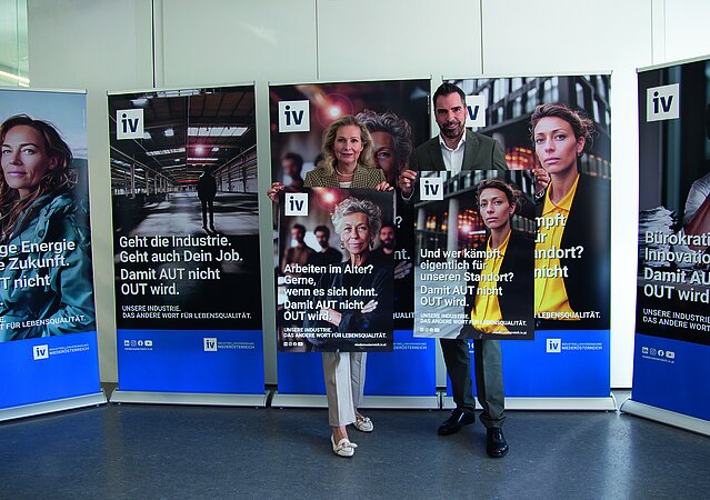 Zwei Personen, IV-NÖ-Geschäftsführerin Michaela Roither (links) und IV-NÖ-Präsident Kari Ochsner (rechts) stehen vor fünf aufgestellten Roll-Ups mit Botschaften der IV-Kampagne „Damit AUT nicht OUT wird“; sie halten jeweils ein Plakat mit Kampagnensujet in den Händen. Die Plakate zeigen unterschiedliche gesellschaftliche und wirtschaftliche Themen rund um Industrie, Arbeit und Standortpolitik.