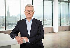 Michael Höllerer, Generaldirektor von Raiffeisen NÖ-Wien, steht im Anzug in einem lichtdurchfluteten Raum mit Blick auf die Wiener Skyline im Hintergrund.
