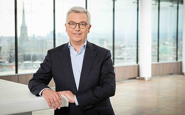 Michael Höllerer, Generaldirektor von Raiffeisen NÖ-Wien, steht im Anzug in einem lichtdurchfluteten Raum mit Blick auf die Wiener Skyline im Hintergrund.