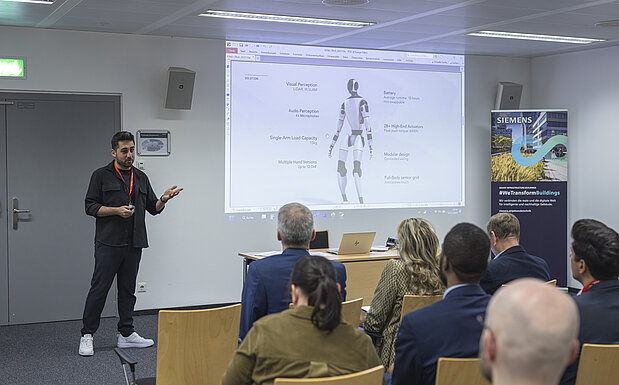 Ein Vortragender präsentiert vor Teilnehmerinnen und Teilnehmern der IV-NÖ-Fokusgruppe „Künstliche Intelligenz & Digitalisierung“ konkrete Anwendungen humanoider Robotik; im Hintergrund eine Präsentationsfolie mit technischen Spezifikationen, aufgenommen in der Siemens City Wien.