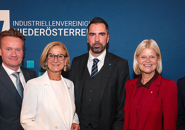 Gruppenfoto beim „Tag der NÖ Industrie“ vor einem Roll-up der Industriellenvereinigung Niederösterreich: (v.l.n.r.) IV-NÖ-Geschäftsführerin Michaela Roither, IV-Präsident Georg Knill, Niederösterreichs Landeshauptfrau Johanna Mikl-Leitner, IV-NÖ-Präsident Kari Ochsner, Verteidigungsministerin Klaudia Tanner und Wirtschaftsminister Wolfgang Hattmannsdorfer stehen nebeneinander und blicken in die Kamera.