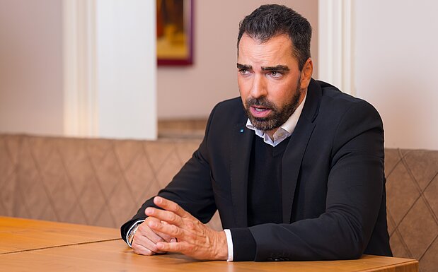 IV-NÖ-Präsident Kari Ochsner im Gespräch, sitzend an einem Tisch, im dunklen Anzug mit weißem Hemd und dunklem Pullover.